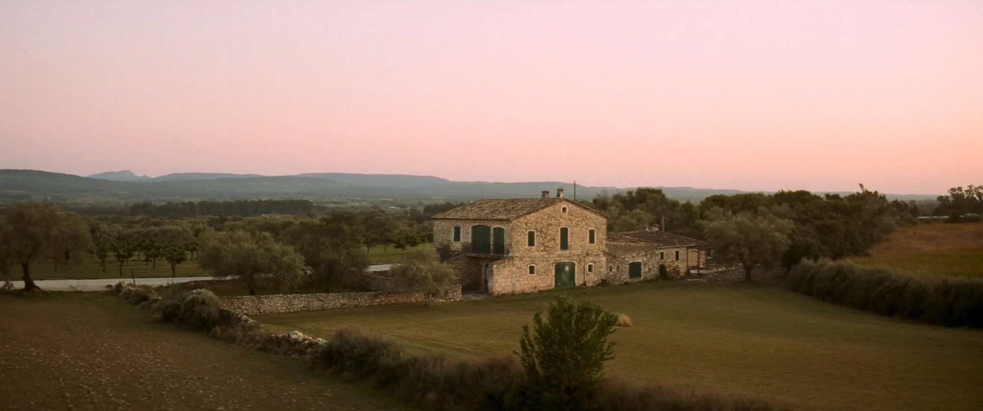 Alte Natursteinfinca mit grünen Fensterläden im Abendlicht, dahinter die Berge Mallorcas